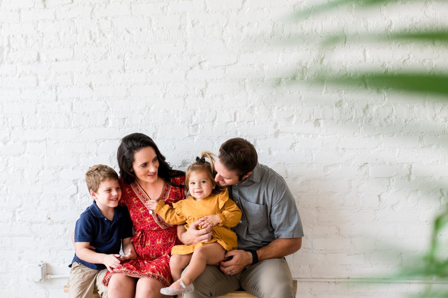 family sitting on a bench in front of white brick wall