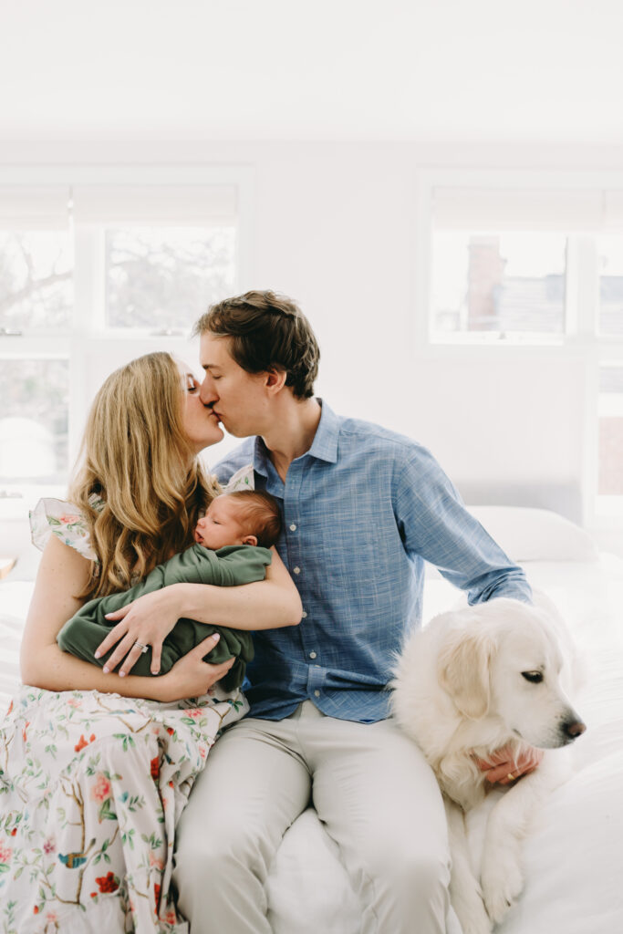 mom and dad kissing while holding baby