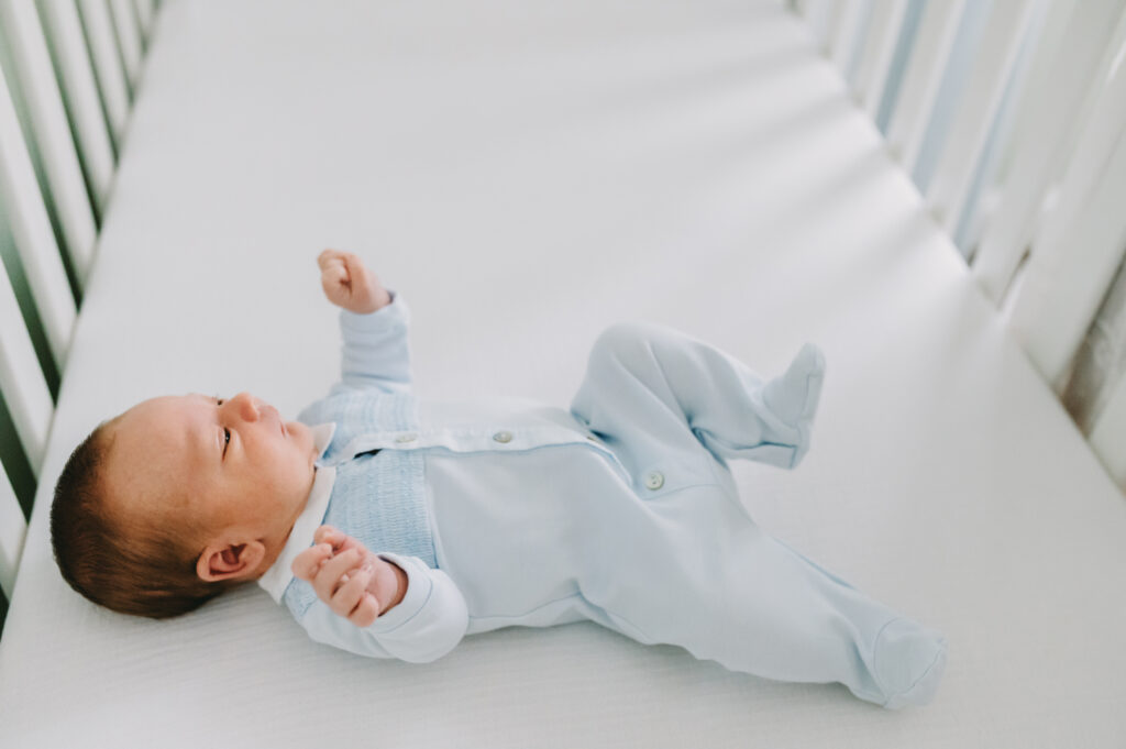 baby boy in blue sleeper in crib