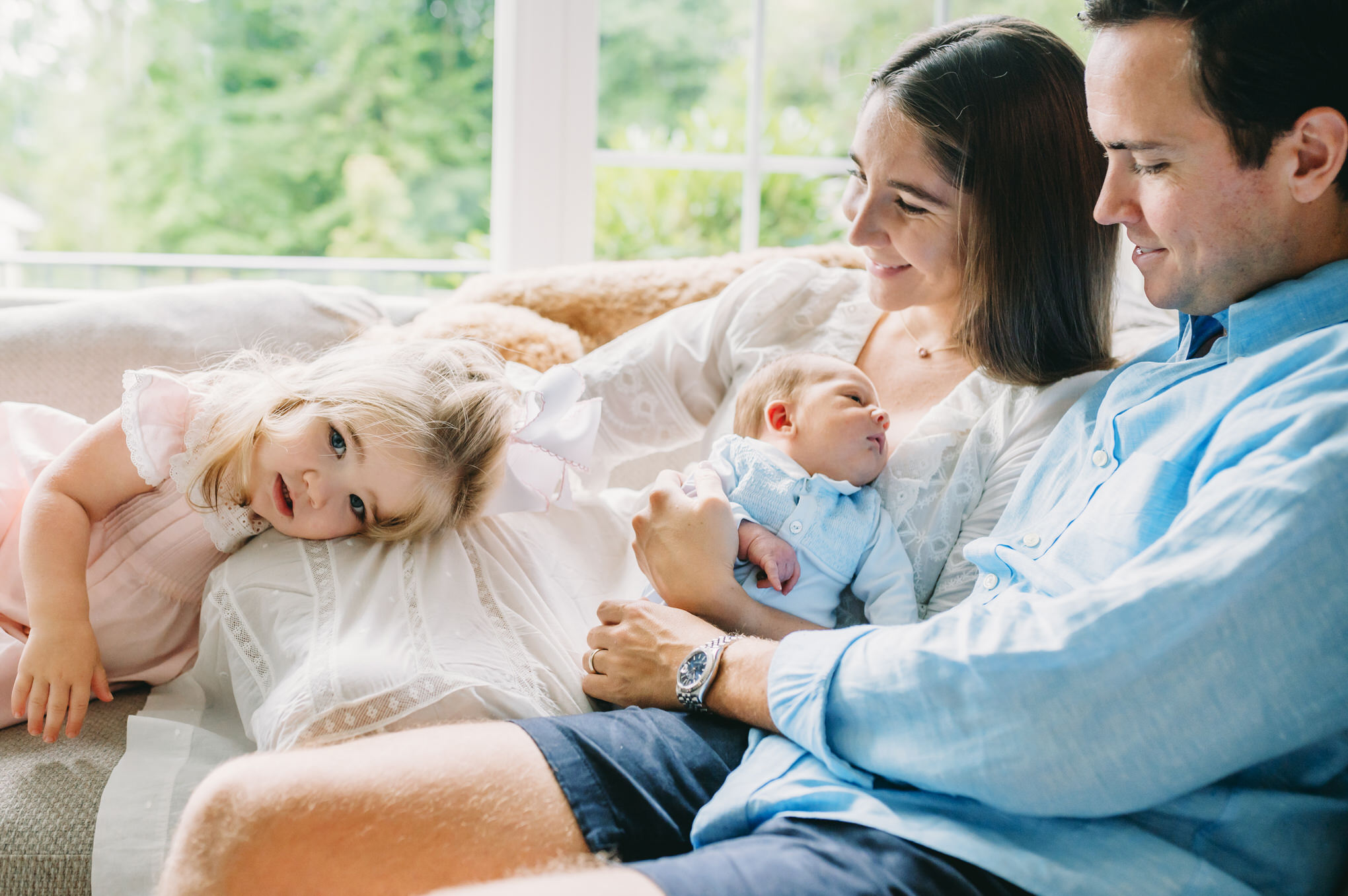 mother and father with newborn and toddler on a sofa