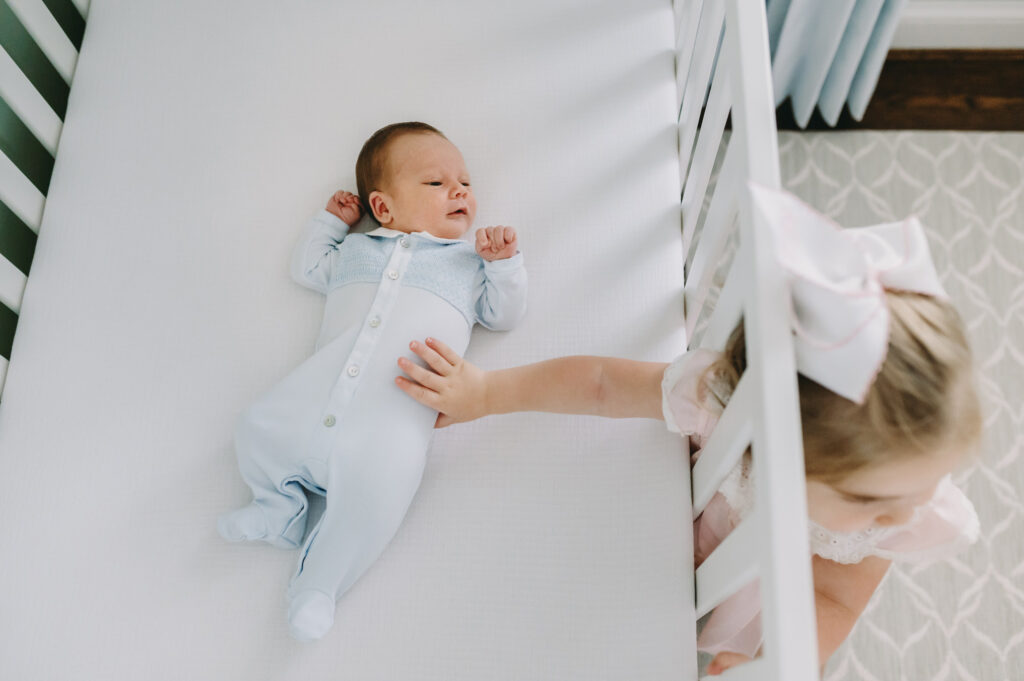 little girl touching baby brother through crib