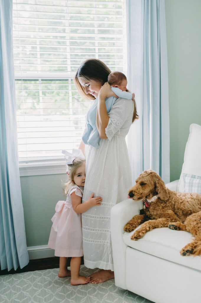 mom holding newborn baby with toddler hugging her legs