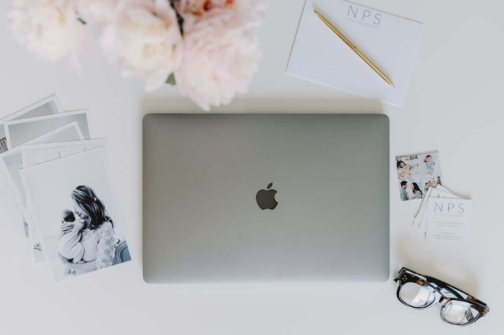 a macbook, glasses, flowers and a newborn session photo and various other accessories on a white background