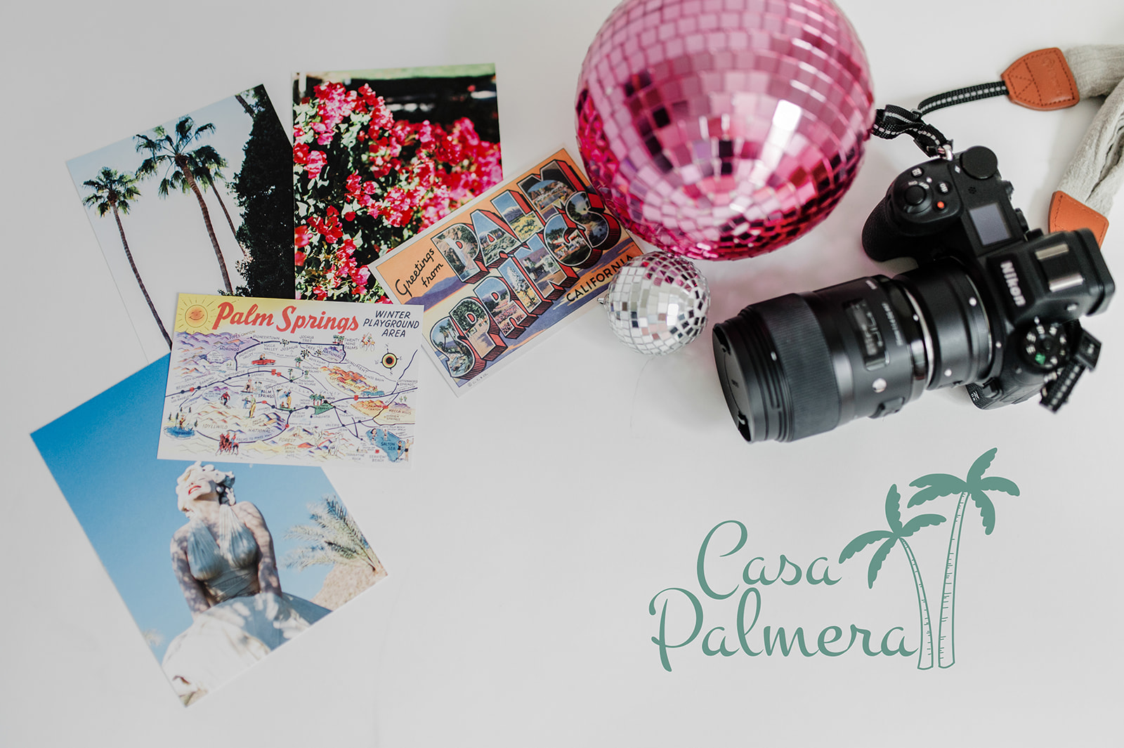 Flat lay of Palm Springs postcards, disco balls, and a camera with "Casa Palmera" text.