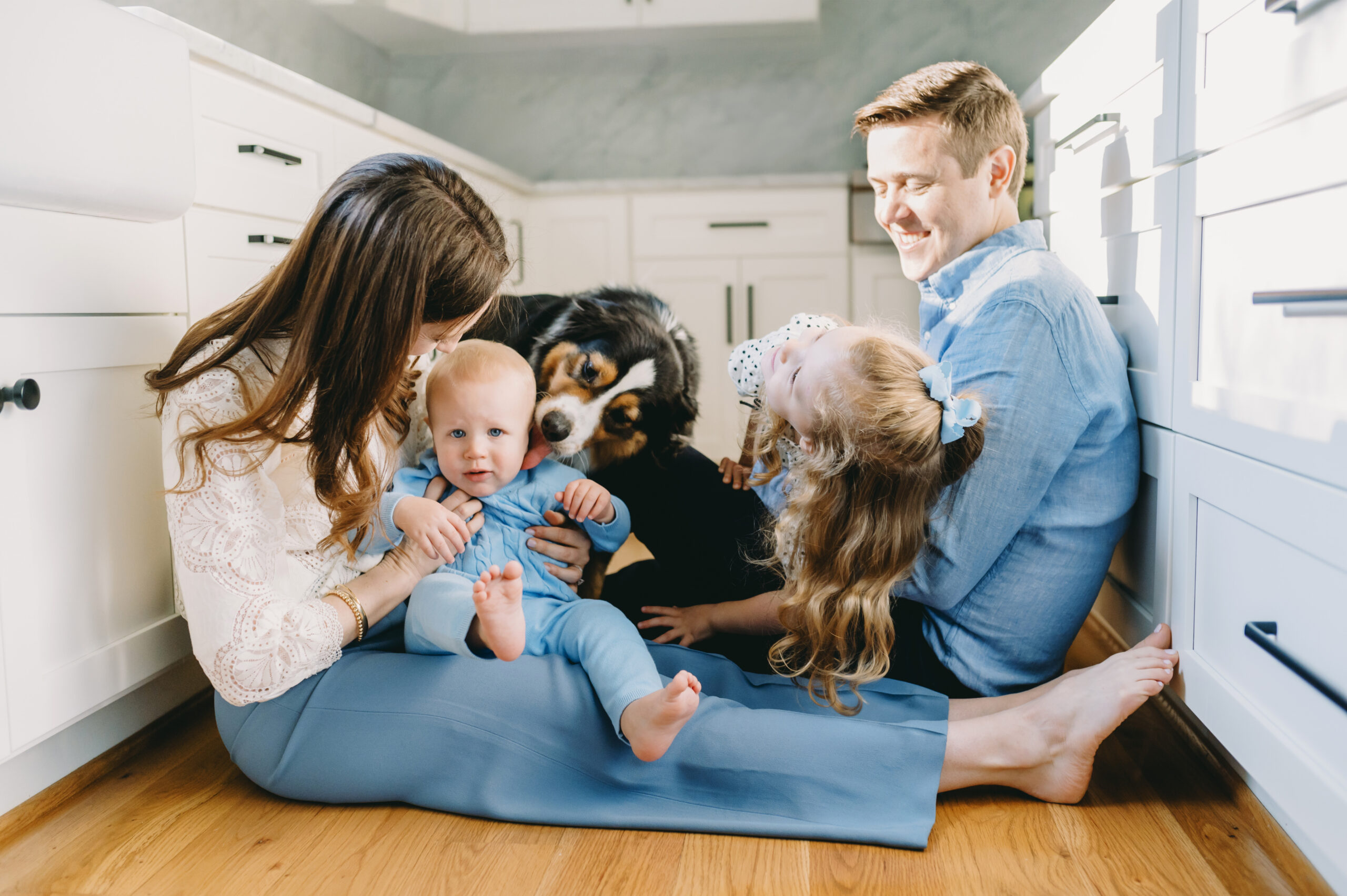 Family Photo Shoot Tips (No Bribes, Just Real Happy Moments) - NPS Photography family sitting in the kitchen with there two kids and pup - family photo shoot tips