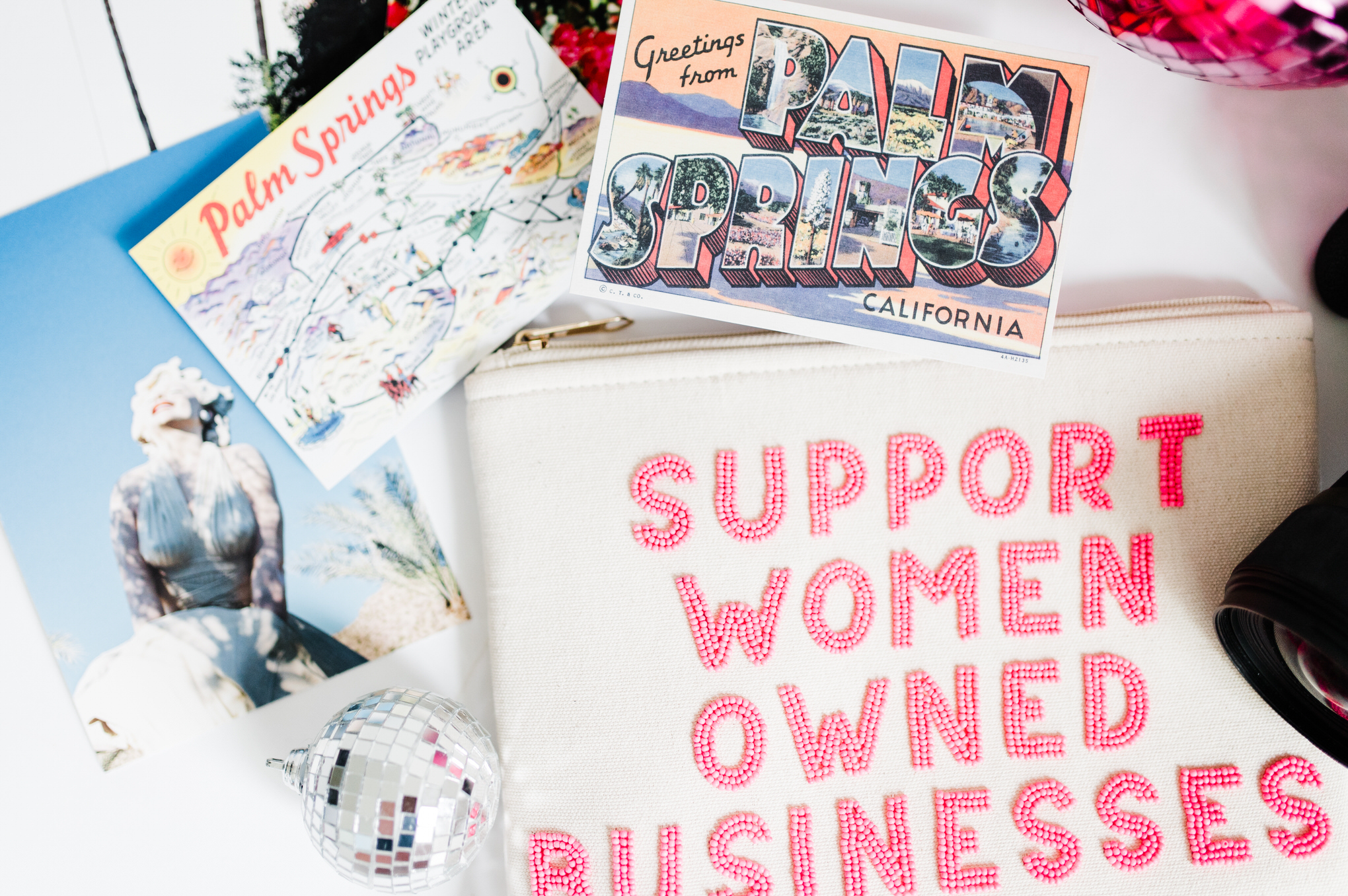 attending-a-photography-retreat Colorful flat lay featuring Palm Springs postcards, vintage photo, disco ball, and "Support Women Owned Businesses" pouch.