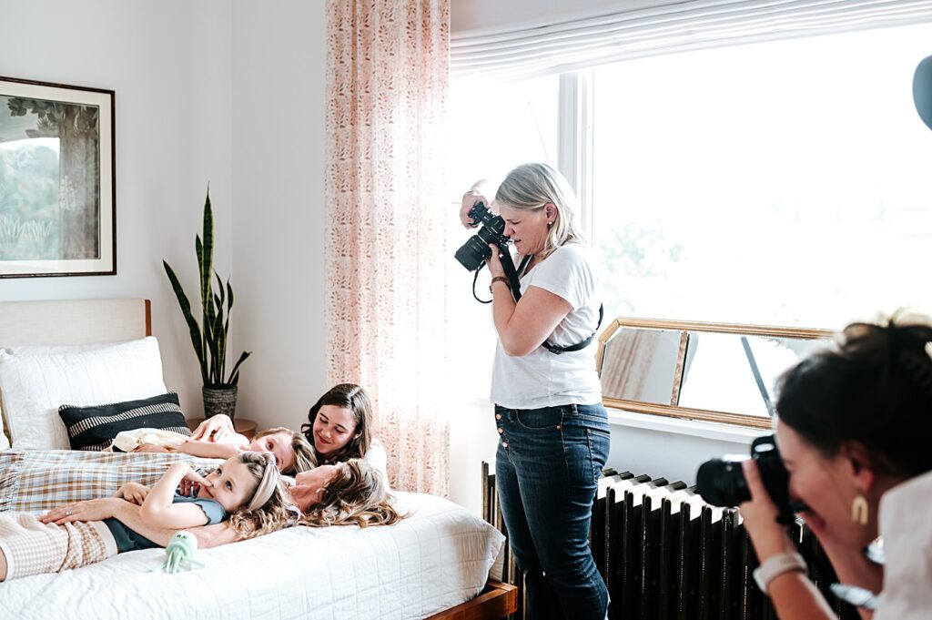 attend-a-photography-retreat Two photographers capture a cozy, candid moment of a mother and daughters snuggling together on a bed while attending a photography retreat
