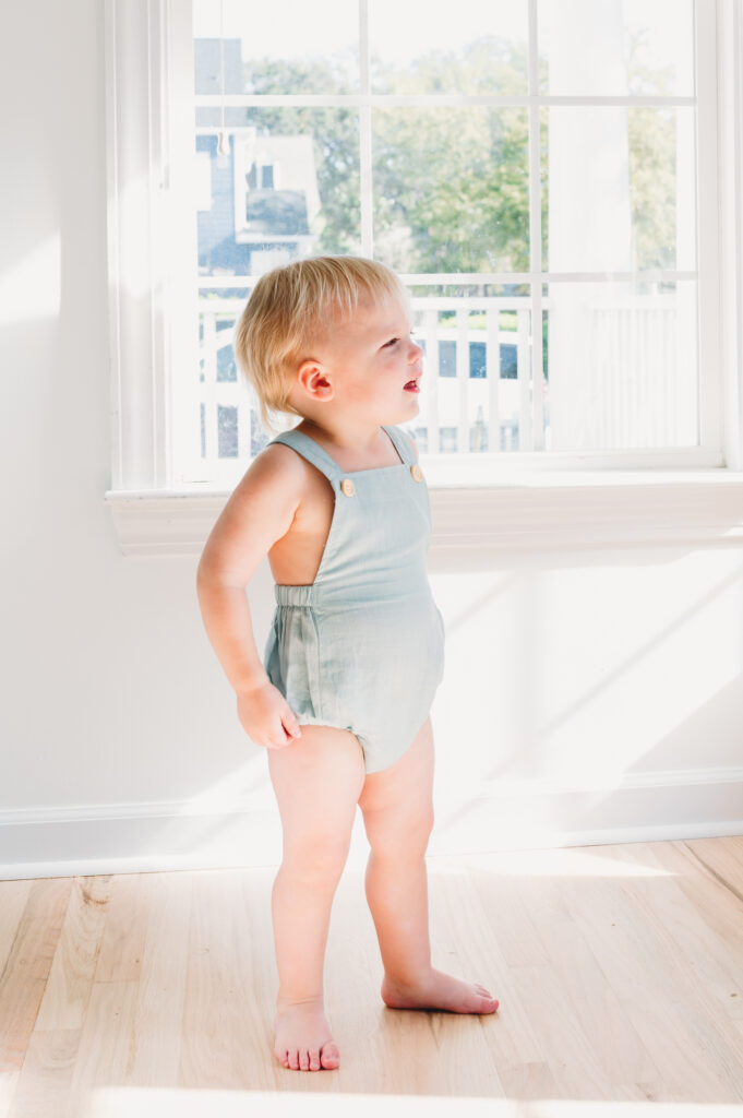 Summer-family-photography-in-DC A curious toddler in a light romper stands bathed in sunlight during a peaceful summer family photography in DC session.