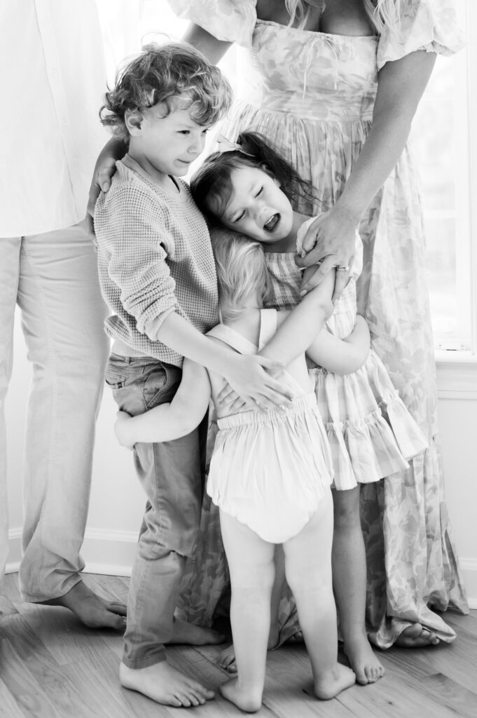 Summer-family-photography-in-DC A heartfelt black-and-white moment of children embracing in a warm family hug with their mother nearby.