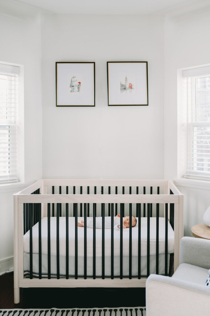 in-home-photo-shoot A peacefully sleeping newborn rests in a modern, minimalist crib bathed in soft natural light.