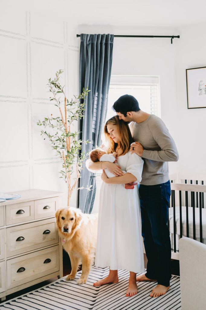 in-home-photo-shoot A loving family shares a tender moment with their newborn and dog during a bright in-home photo shoot.