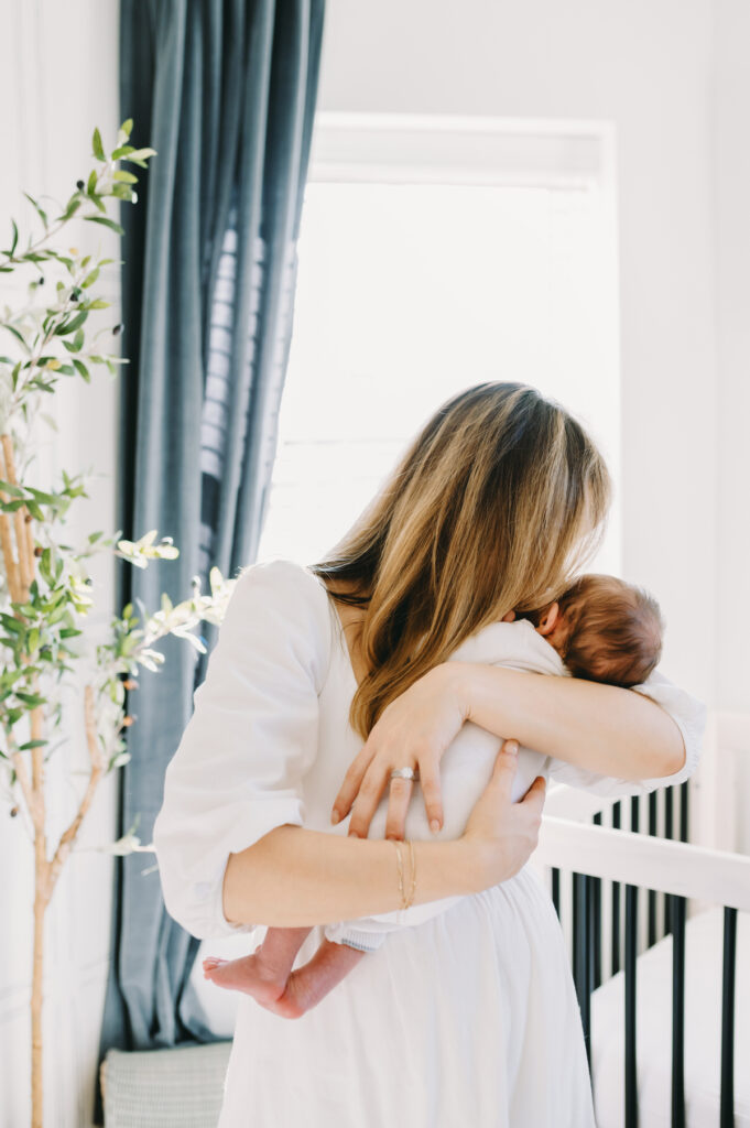 in-home-photo-shoot A mother lovingly holds her newborn close during a tender, natural in-home photo shoot filled with soft light.