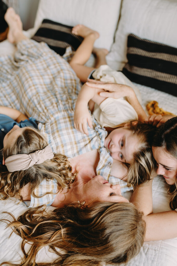 photography-prompts-for-kids A tender moment of a mother lying on the bed, surrounded by her children sharing laughter and closeness.