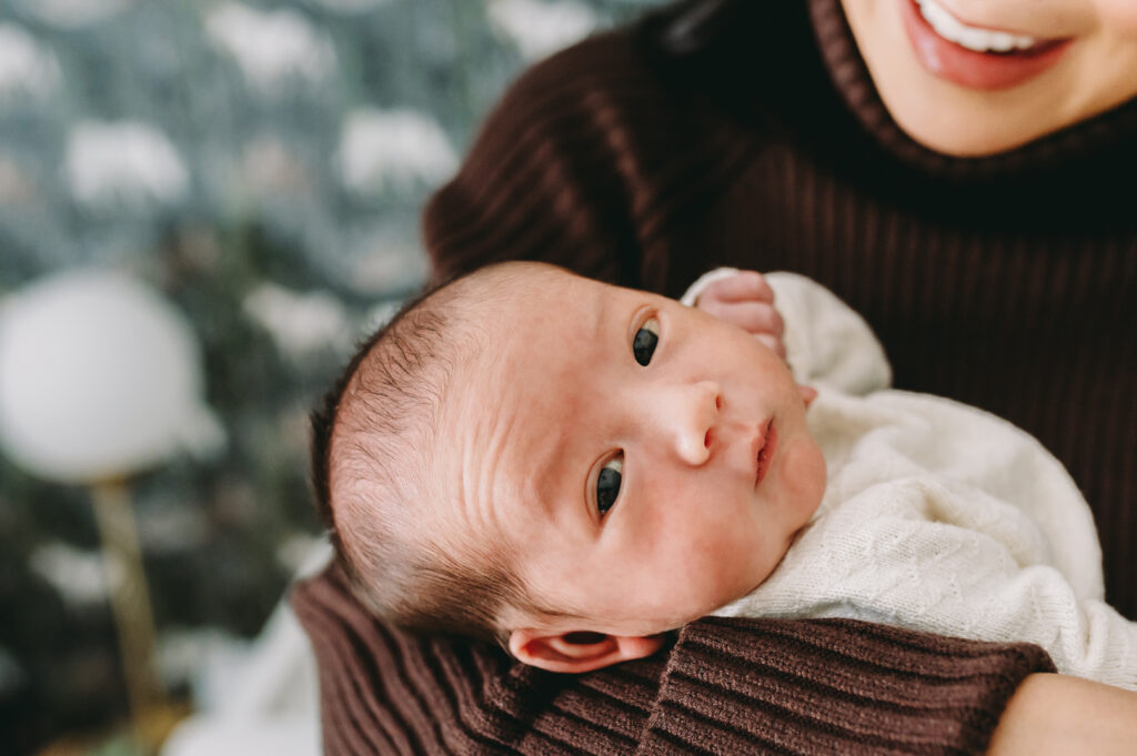 Lifestyle Newborn Session vs. Studio: Which One Fits Your Family Best? - NPS Photography Newborn baby looking up while being held during an intimate lifestyle newborn session in the nursery.