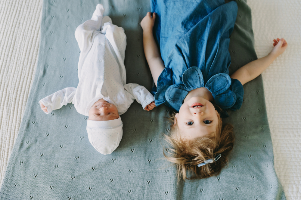 Newborn and Sibling Photography: Capturing Candid Moments at Home - NPS Photography Toddler girl and newborn baby lying side-by-side on a blanket during a cozy at-home newborn and sibling photography session.