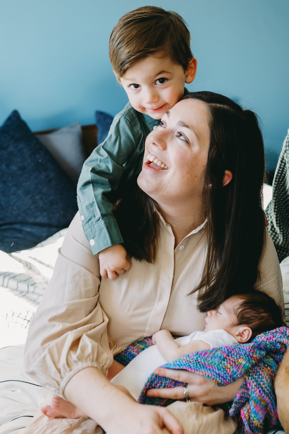 A loving mom smiles at her toddler while holding a newborn during an in-home session—photography ideas in home that highlight genuine connection.