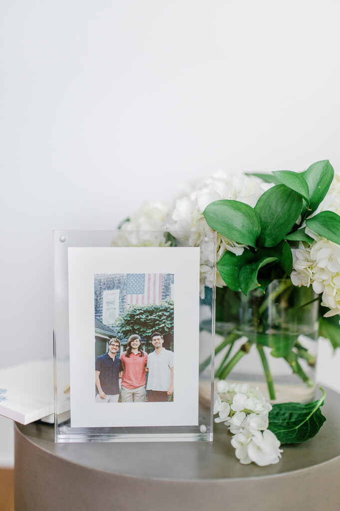 Heirloom photography display featuring a matted print in a modern acrylic frame beside fresh white flowers.