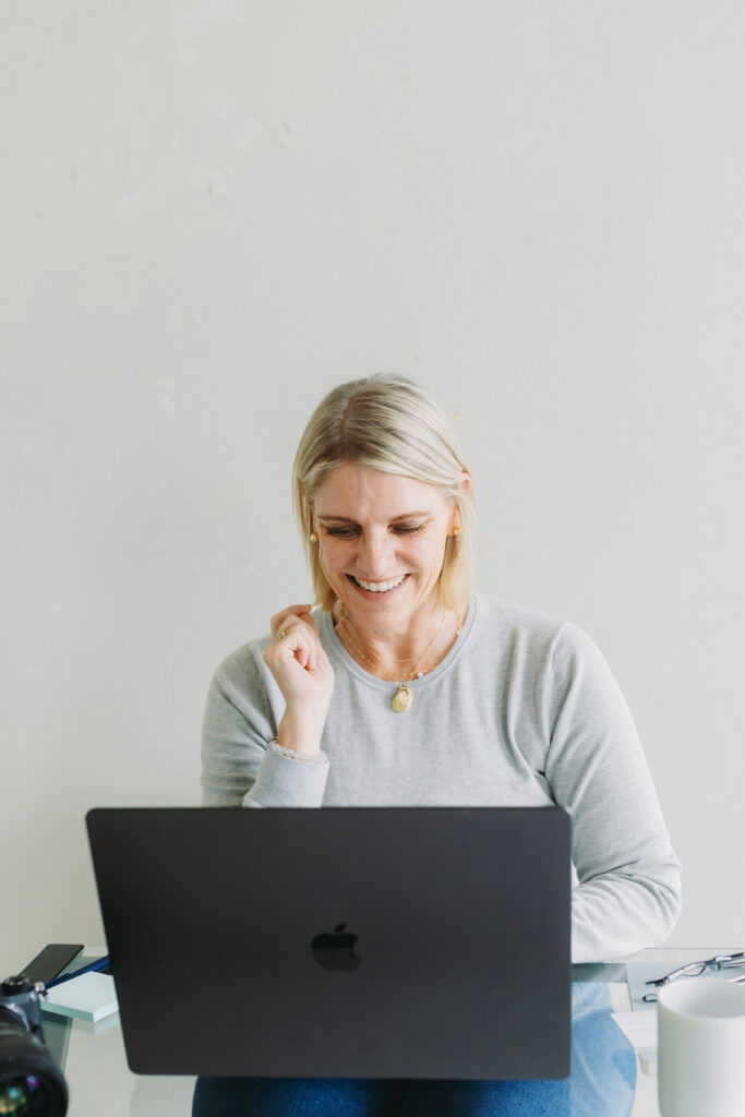 How to Create a Photography Website That Attracts Dream Clients - NPS Photography Woman smiling at laptop while working, embodying the joy of discovering how to create a photography website that works.