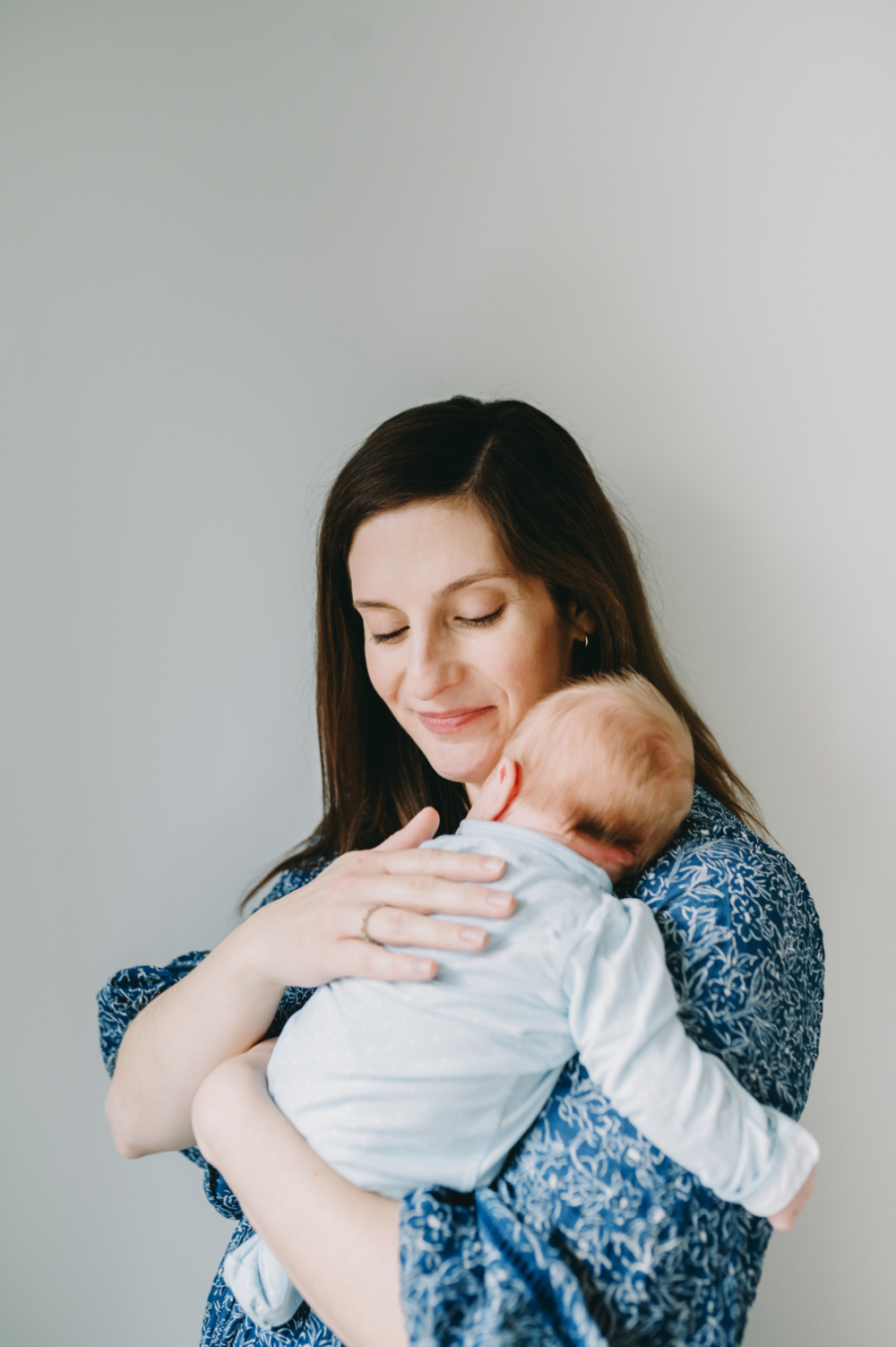 A quiet, heartfelt motherhood photography portrait of a mother holding her newborn close with eyes closed in a peaceful embrace.
