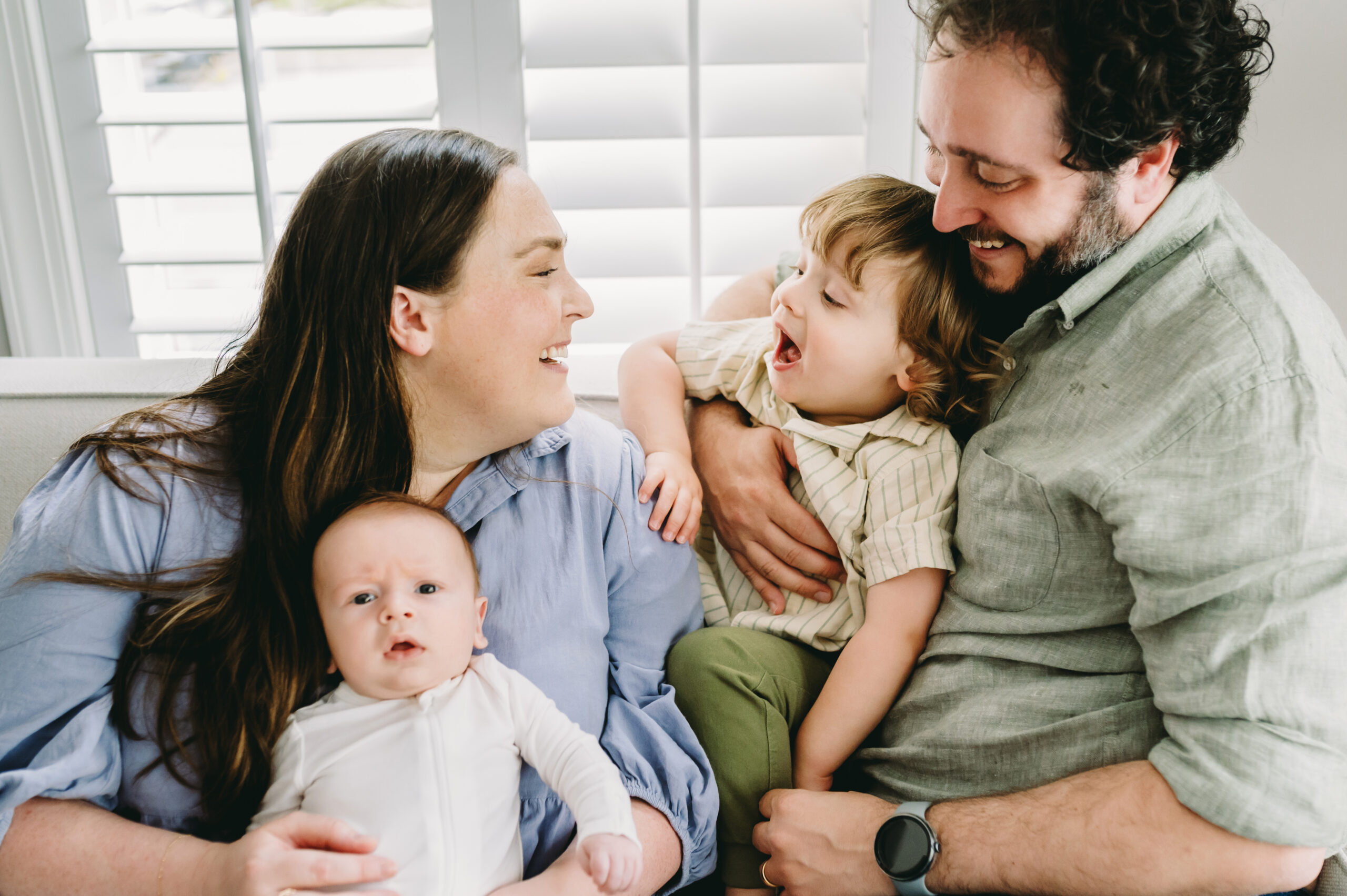 Indoor Winter Family Photos: A Cozy Home Prep Guide - NPS Photography A family of four sharing laughter and connection on the couch, illuminated by window light during indoor winter family photos.