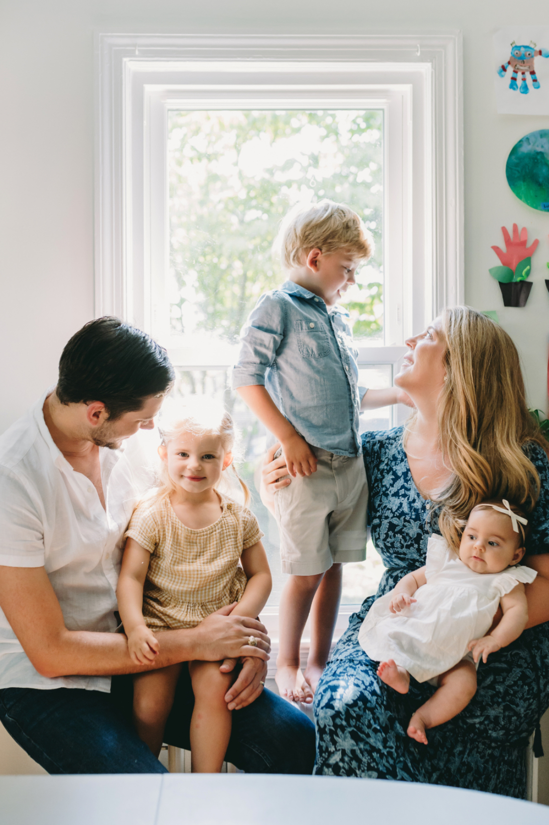 A family gathered around a bright window, wearing coordinated family picture outfits in soft, natural tones for a warm, cohesive look.
