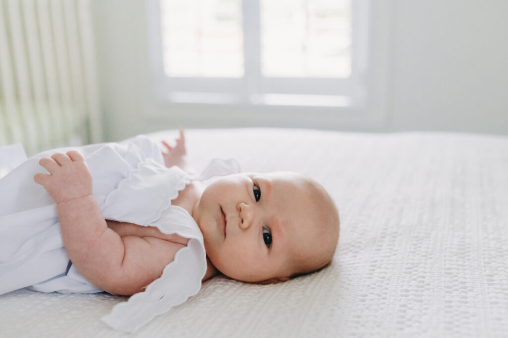 Family Picture Outfits: Your Guide to the Best Photography Looks in the DMV - NPS Photography A newborn resting on a softly lit bed in a white romper, a timeless choice for family picture outfits during in-home sessions.