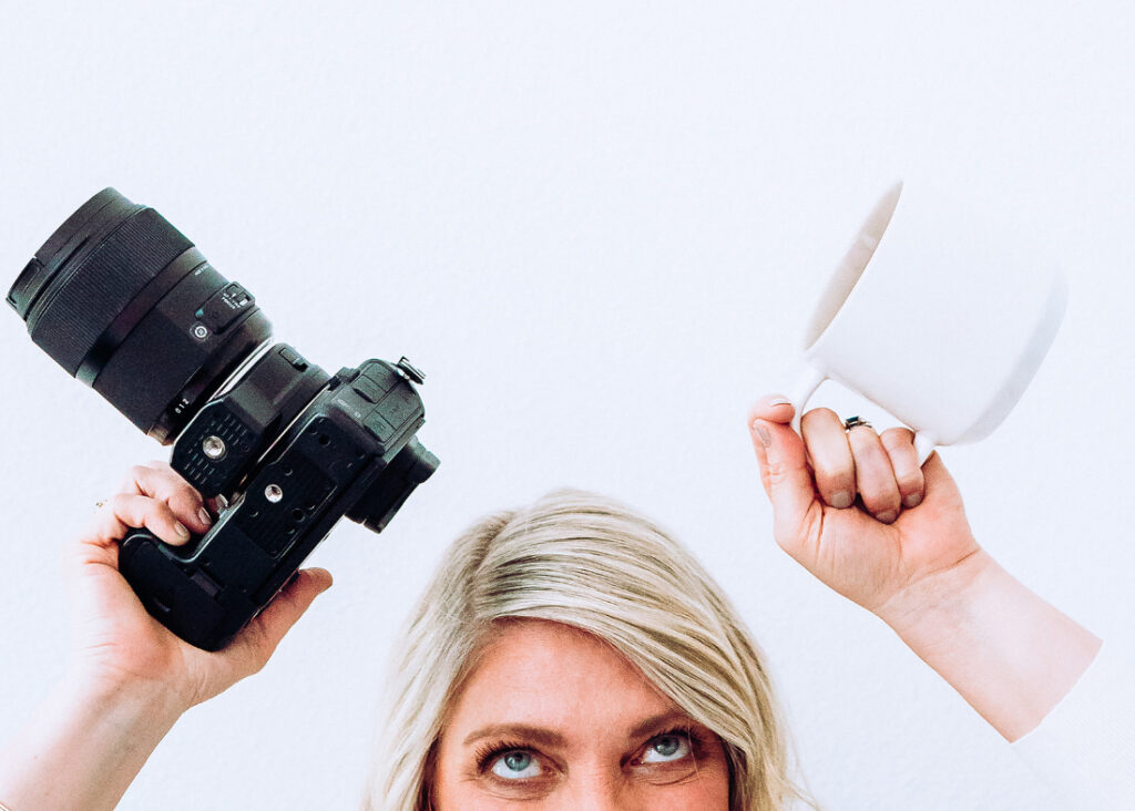 A playful portrait of a photographer holding up a camera and coffee mug, symbolizing the balance encouraged in photography business tips for avoiding burnout.
