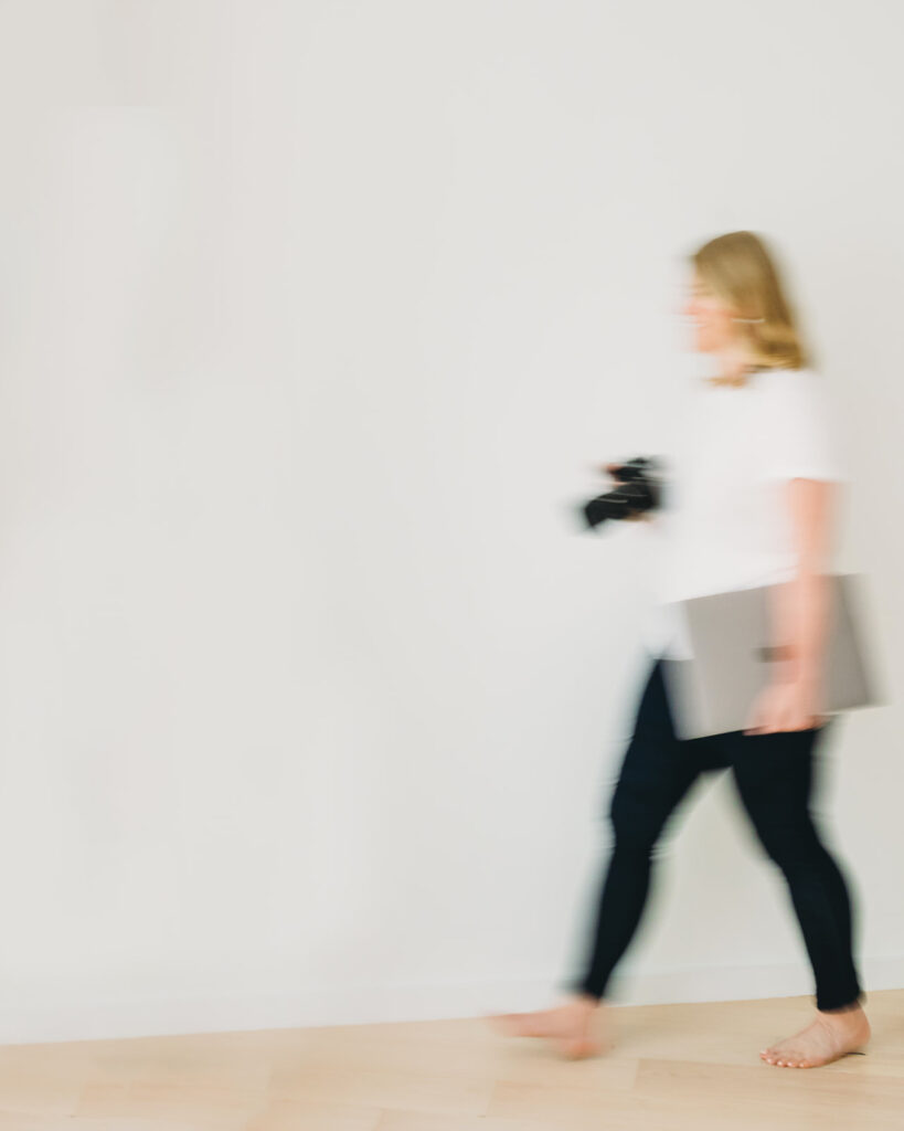 A blurred motion image of a photographer walking with camera and laptop in hand, representing photography business tips about managing workflow and staying organized.