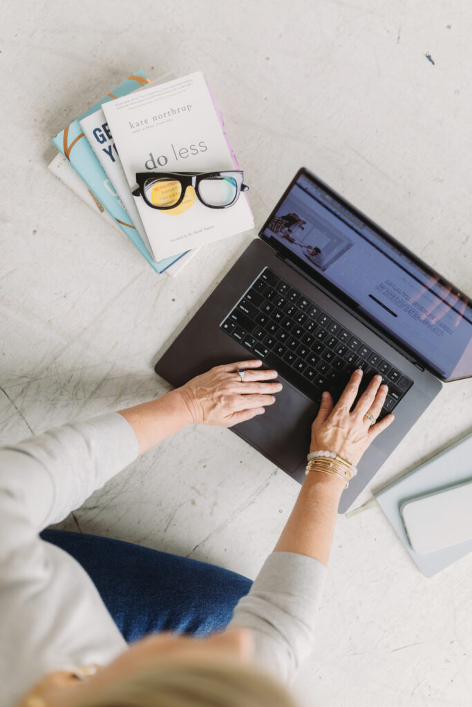 An overhead view of hands typing on a laptop beside business books, illustrating photography business tips focused on planning, systems, and year-end review.