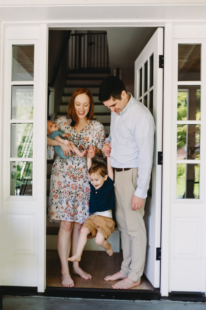 What Is Storytelling Photography? The Heartfelt Secret to Capturing Your Family’s Most Meaningful Moments - NPS Photography Parents standing in their doorway with their newborn and older child, illustrating what is storytelling photography through natural family interaction.