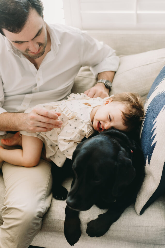 little girl with dad hugging black lab